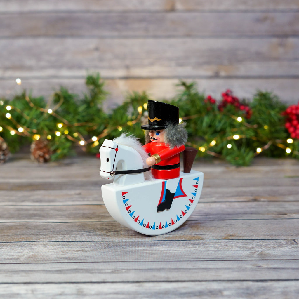 Nutcracker on red rocking horse amid Christmas background