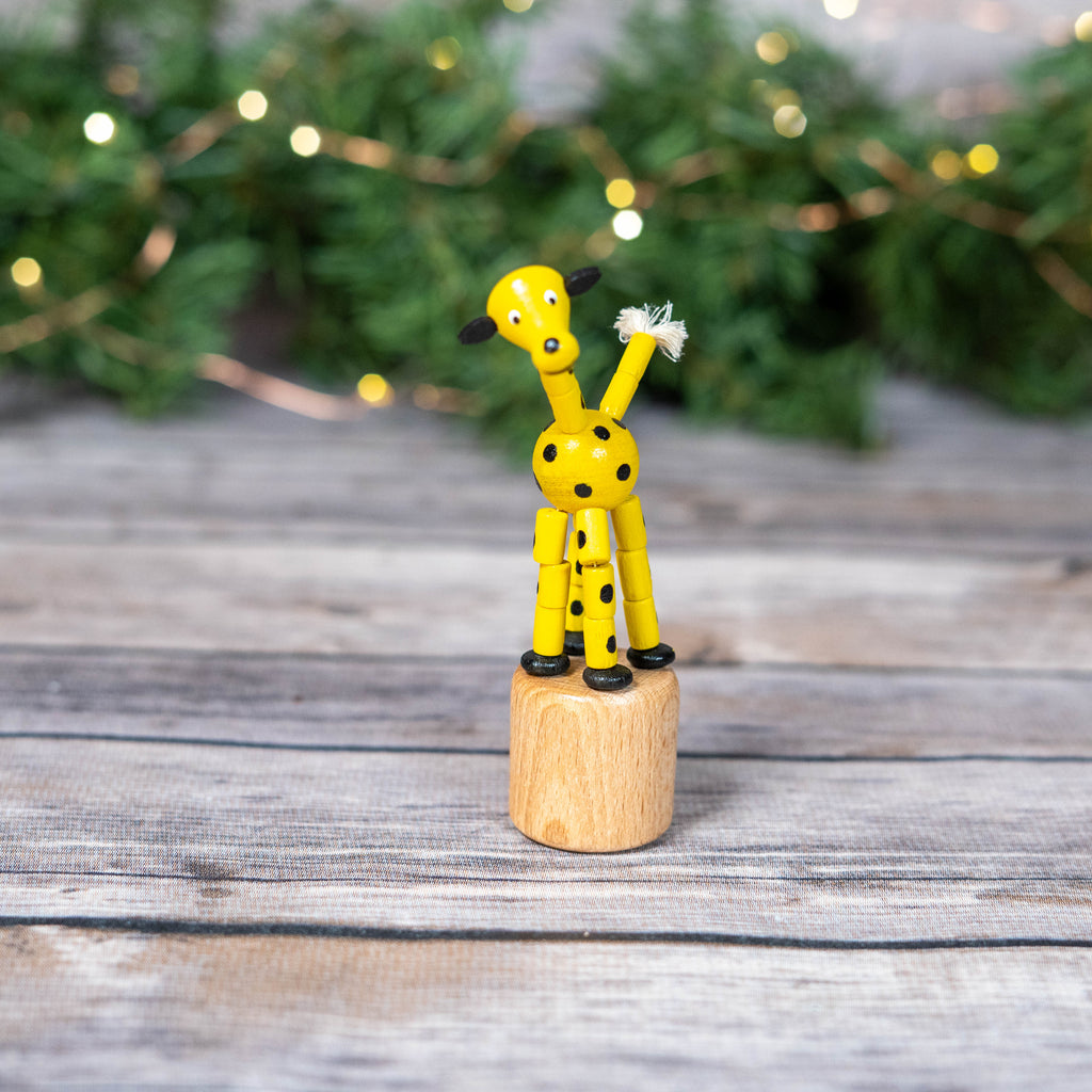 Wobbly giraffe toy on wooden stump with Christmas lights in the background